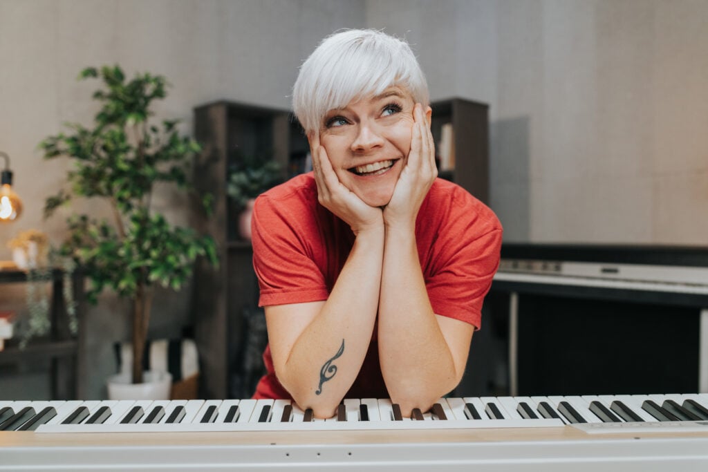 Woman with short platinum hair smiling with elbows on a keyboard and chin in hands.