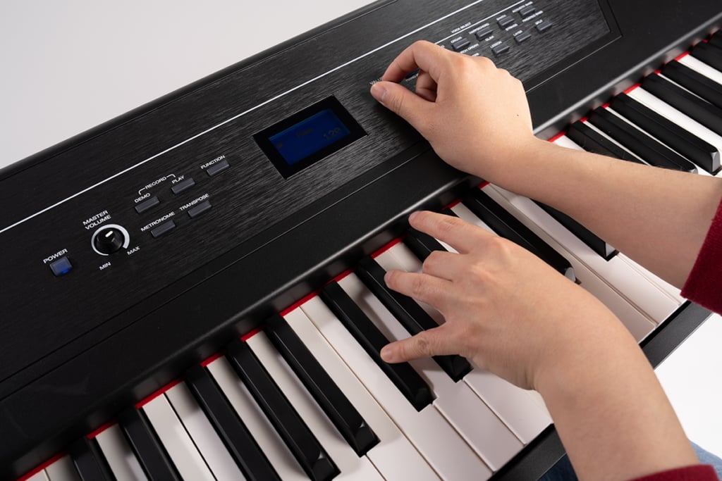 Hands on digital piano keyboard with left hand playing and right hand fiddling with buttons.