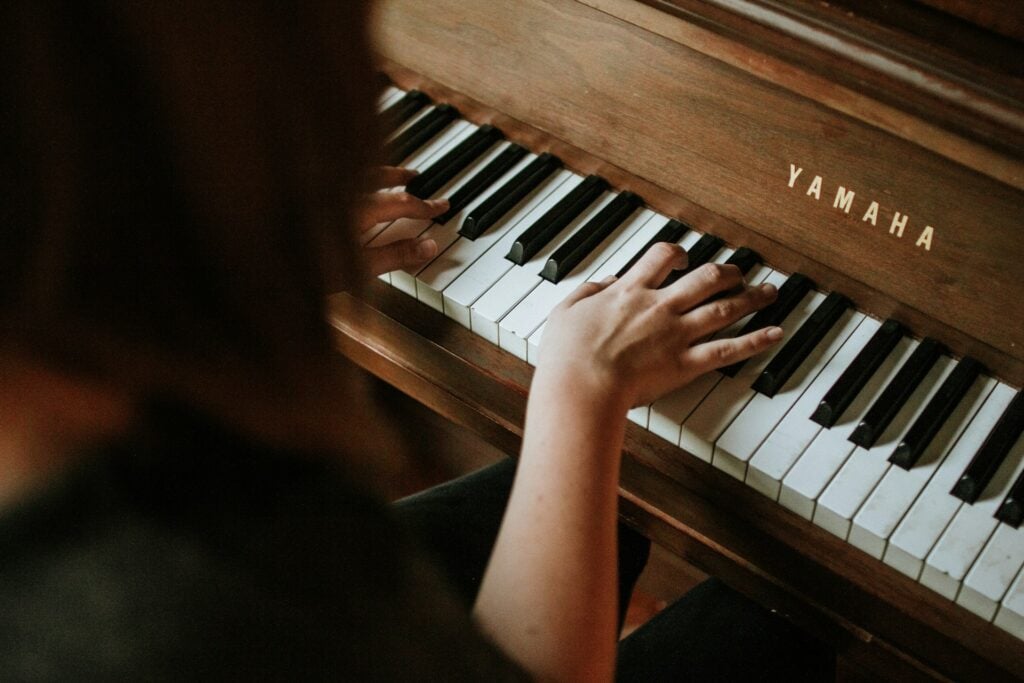 Overhead view of hands playing acoustic upright piano keys of a brown wood finish piano. How to clean a piano.